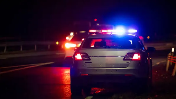 A patrol car on a dark highway shoulder with its light bar running.