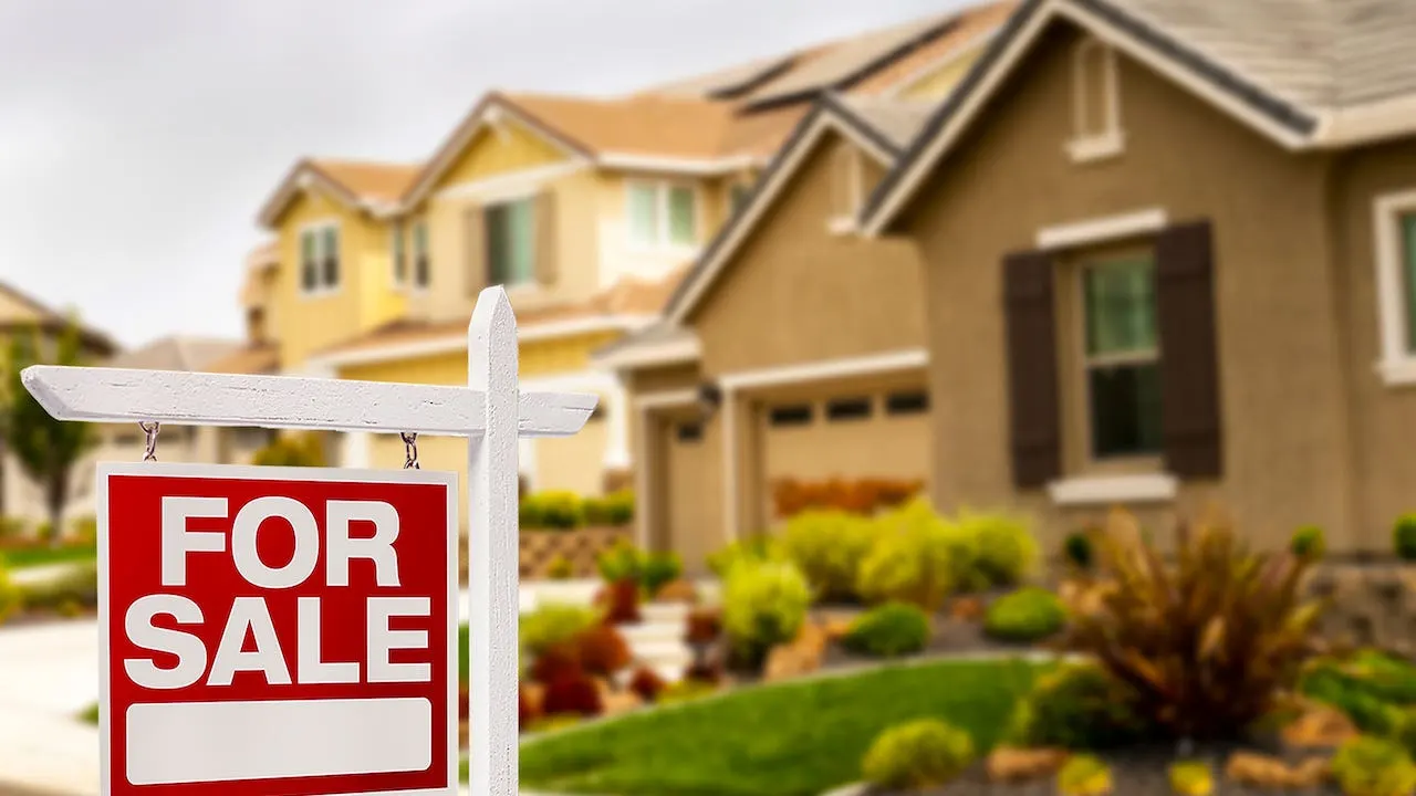 A For Sale sign on the lawn of a suburban house.